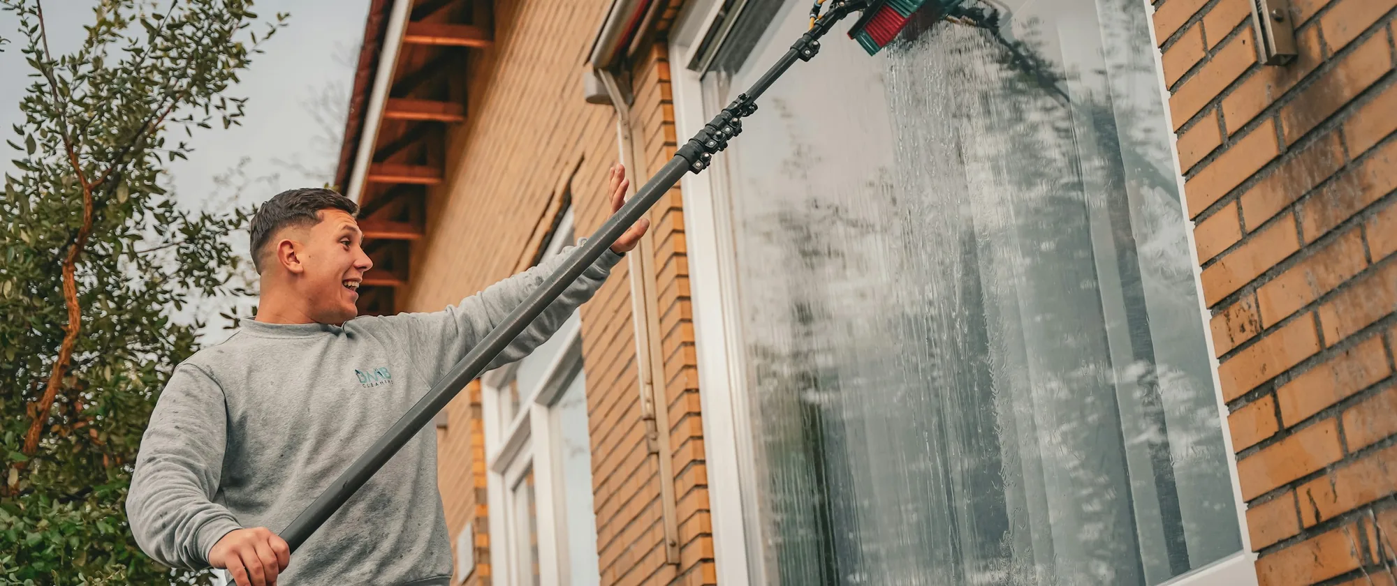 Fönsterputsare tvättar fönster med teleskopstång på ett tegelhus