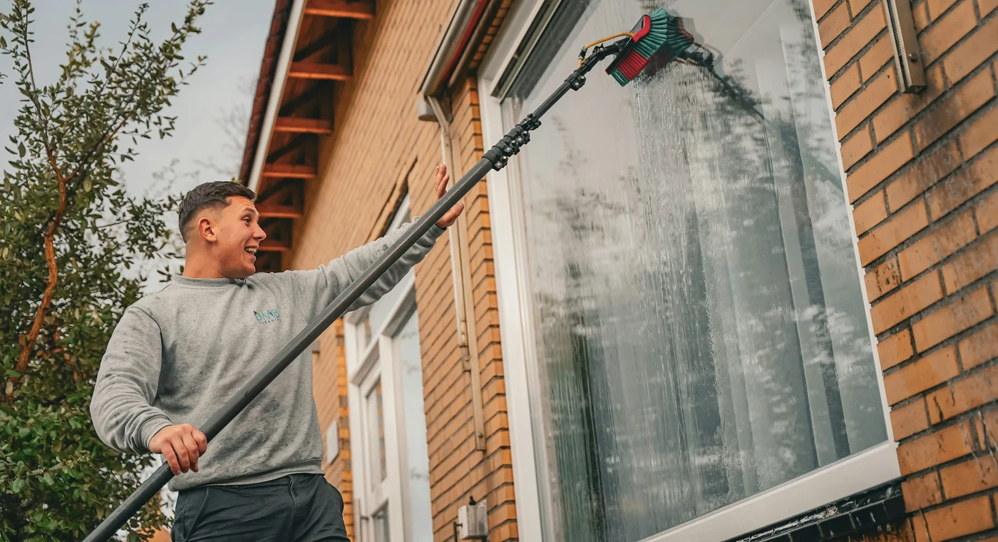 Fönsterputsare tvättar fönster med teleskopstång på ett tegelhus